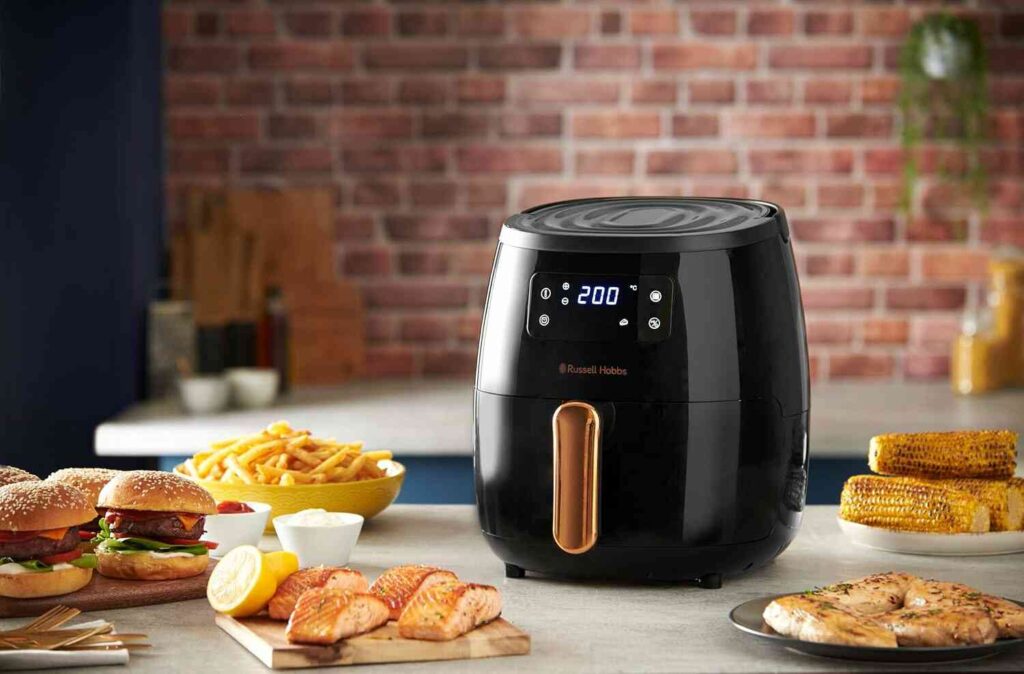 Russell Hobbs Airfryer 26510-56 Sienna na kuhinjskom stolu sa hranom pripremljenom u fritezi na vruć vazduh